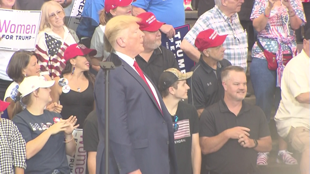 Pres Trump looks up into the arena crowd at some protestors being escorted out after interupting his speech